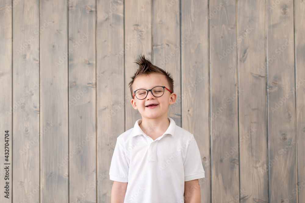 Portrait of little boy laughing in glasses and white T-shirt at wooden background. Preparation for school. having an idea. No milk teeth. Low vision, eyesight measurement. Back to school. Portrait of little boy laughing in glasses and white T-shirt at wooden background. Preparation for school. having an idea. No milk teeth. Low vision, eyesight measurement. Back to school.