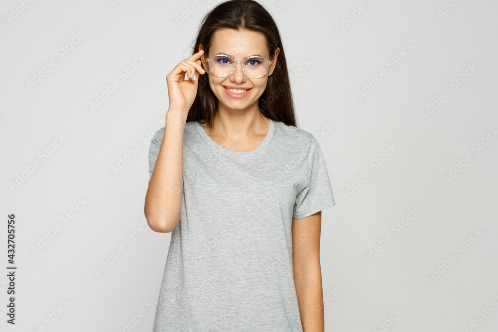 Beautiful girl in casual t-shirt and glasses. Gray background. Portrait of smiling young woman.