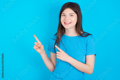 young beautiful Caucasian woman wearing blue T-shirt over blue wall points at copy space indicates for advertising gives right direction
