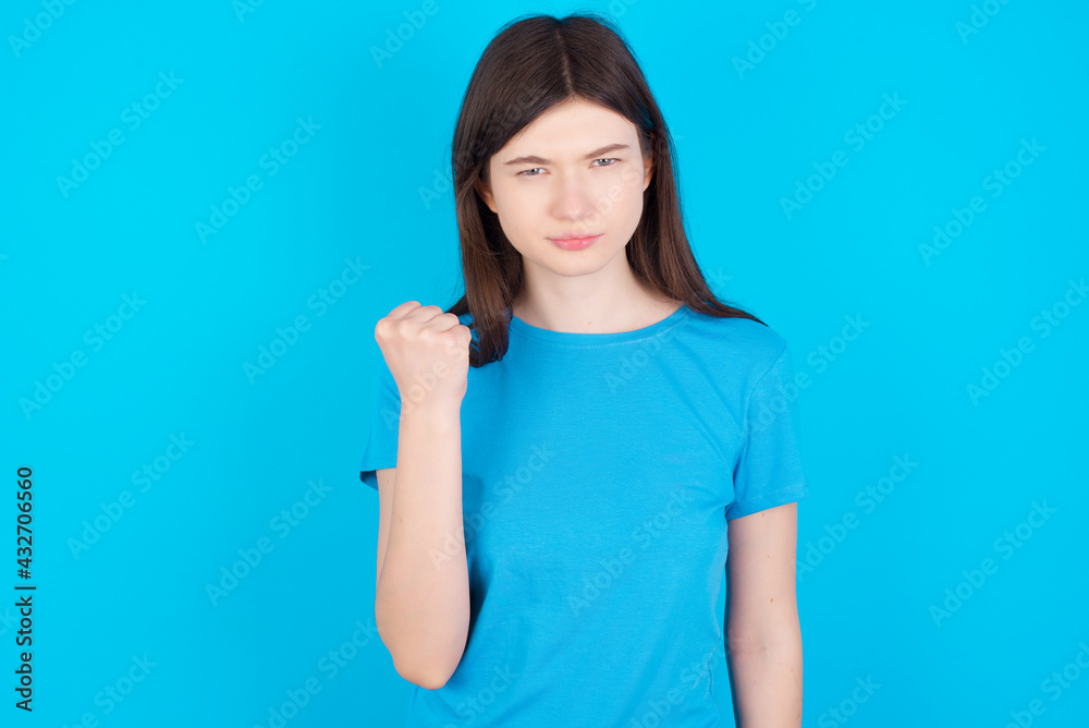 young beautiful Caucasian woman wearing blue T-shirt over blue wall shows fist has annoyed face expression going to revenge or threaten someone makes serious look. I will show you who is boss young beautiful Caucasian woman wearing blue T-shirt over blue wall shows fist has annoyed face expression going to revenge or threaten someone makes serious look. I will show you who is boss