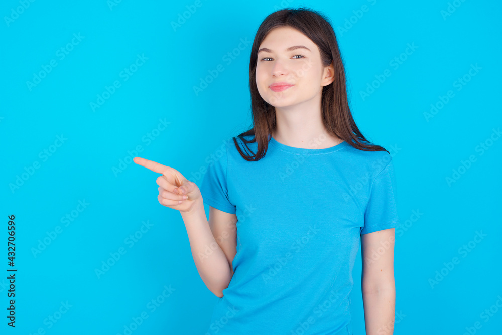 young beautiful Caucasian woman wearing blue T-shirt over blue wall points to side on blank space demonstrates advertisement. People and promotion concept young beautiful Caucasian woman wearing blue T-shirt over blue wall points to side on blank space demonstrates advertisement. People and promotion concept