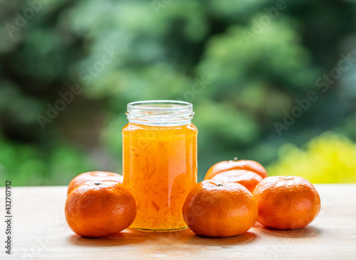 Jar of orange marmalade no label and orange fruits with blurred natural green background