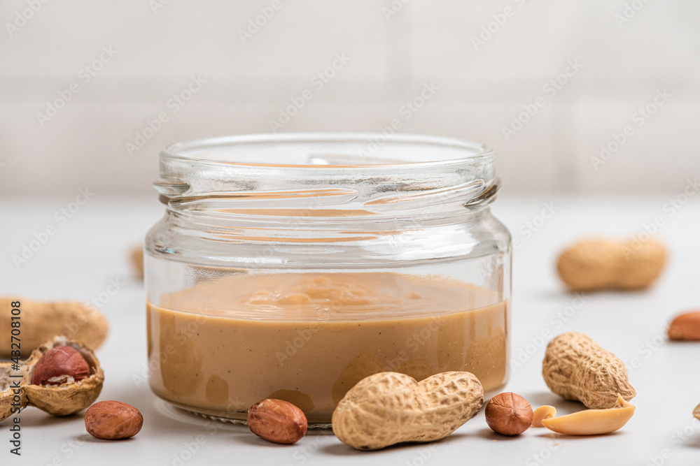 Peanut butter jar and heap of nuts on white background. Organic vegan food. Tasty breakfast Peanut butter jar and heap of nuts on white background. Organic vegan food. Tasty breakfast