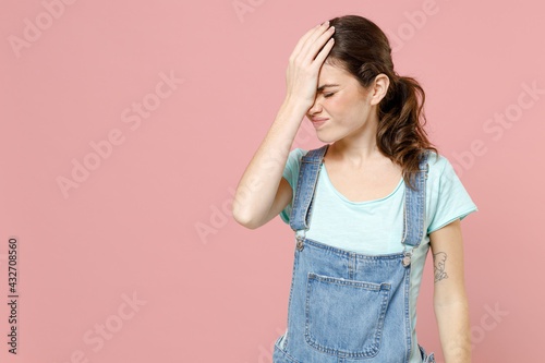 Young ashamed mistaken confused caucasian woman in denim clothes blue t-shirt put hand on face facepalm epic fail gesture isolated on pastel pink background studio portrait People lifestyle concept. photo