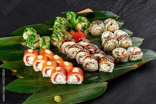 californi sushi set lies on a background of green bamboo leaves on a black background