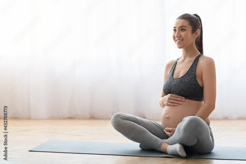 Young expecting woman training on mat at home, getting ready for childbirth
