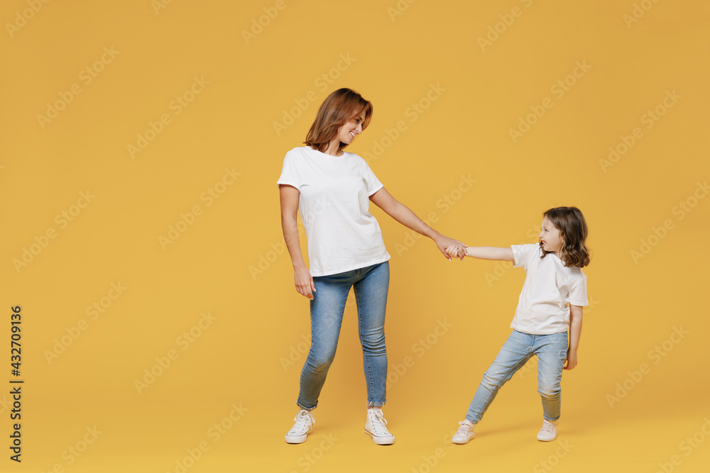 Full length happy woman in basic white t-shirt have fun with cute child baby girl 5-6 years old hold hands. Mom little kid daughter isolated on yellow color background studio Mother's Day love family Full length happy woman in basic white t-shirt have fun with cute child baby girl 5-6 years old hold hands. Mom little kid daughter isolated on yellow color background studio Mother's Day love family