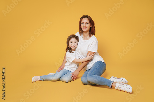 Full body length happy woman in basic white t-shirt have fun sit on floor with child baby girl 5-6 year old Mom little kid daughter isolated on yellow color background studio Mother's Day love family