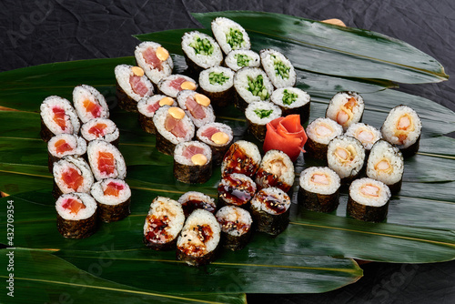 sushi set with tuna, salmon, shrimp, eel and color cucumber lies on a background of green bamboo leaves on a black background
