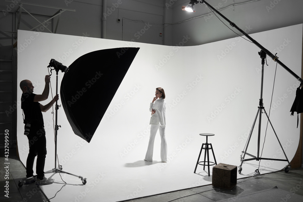 Fashion photography in a photo studio. Professional male photographer taking pictures of beautiful woman model on camera, backstage - obrazy, fototapety, plakaty 