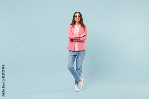 Full length young smiling happy trendy stylish fashionable woman 20s wear pastel pink clothes glasses hold hands crossed folded isolated on blue background studio portrait. People lifestyle concept