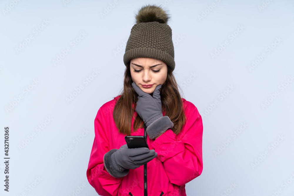 Young girl with winter hat isolated on blue background thinking and sending a message Young girl with winter hat isolated on blue background thinking and sending a message