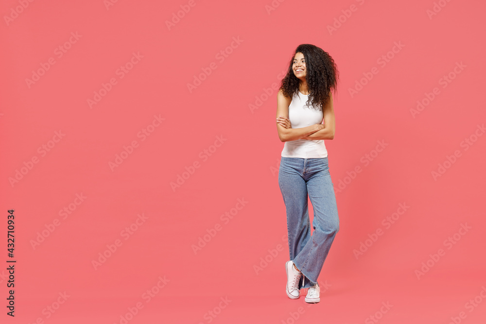 Full length young fun smiling happy friendly positive african american woman 20s wearing white tank shirt hold hands crossed folded look aside isolated on pink background. People lifestyle concept Full length young fun smiling happy friendly positive african american woman 20s wearing white tank shirt hold hands crossed folded look aside isolated on pink background. People lifestyle concept