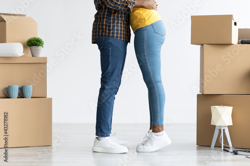Cropped image of black couple embracing among cardboard boxes after relocation