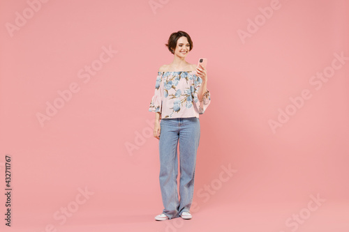 Full length young happy smiling fun fashionable caucasian woman with short hairdo wear trendy stylish blouse hold mobile cell phone chat online isolated on pastel pink color background studio portrait