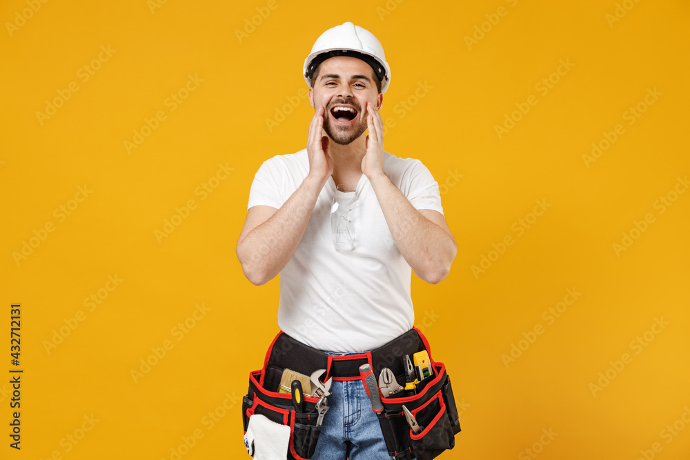 Young excited employee handyman man in protective helmet hardhat scream news with hands near mouth isolated on yellow background Instruments accessories renovation apartment room Repair home concept.