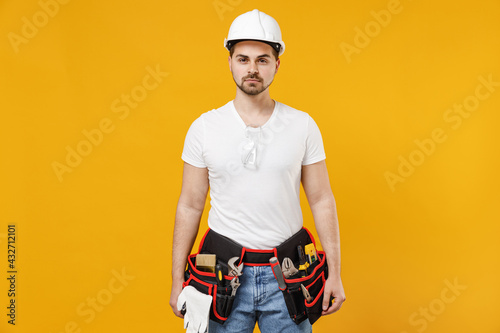 Young confident employee handyman man 20s wearing protective helmet hardhat isolated on yellow background studio portrait. Instruments accessories for renovation apartment room. Repair home concept.