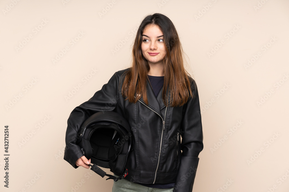 Woman with a motorcycle helmet isolated on beige background standing and looking to the side Woman with a motorcycle helmet isolated on beige background standing and looking to the side