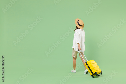 Fotografie Full length rear back view traveler tourist woman in casual clothes hat hold yellow suitcase walking going isolated on green background