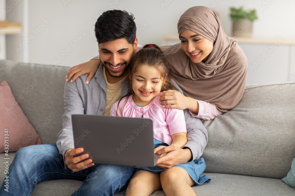 Precious time with family. Happy muslim parents and cute little girl using laptop together, watching photos or movie Precious time with family. Happy muslim parents and cute little girl using laptop together, watching photos or movie