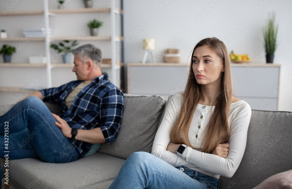 Family disagreement. Angry mature woman and her husband sitting on different ends of sofa at home after quarrel
