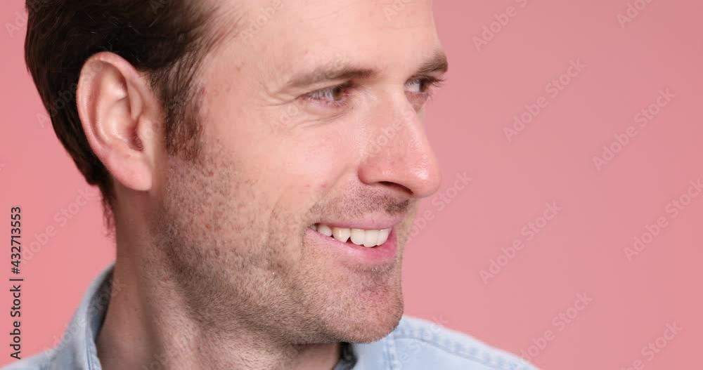 confident young casual man looking to side, smiling and nodding in a close up view on pink background in studio confident young casual man looking to side, smiling and nodding in a close up view on pink background in studio