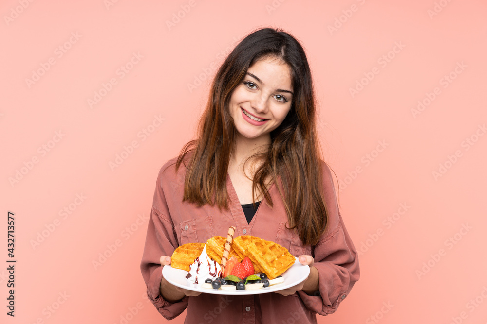 Young caucasian woman holding waffles isolated on pink background smiling a lot