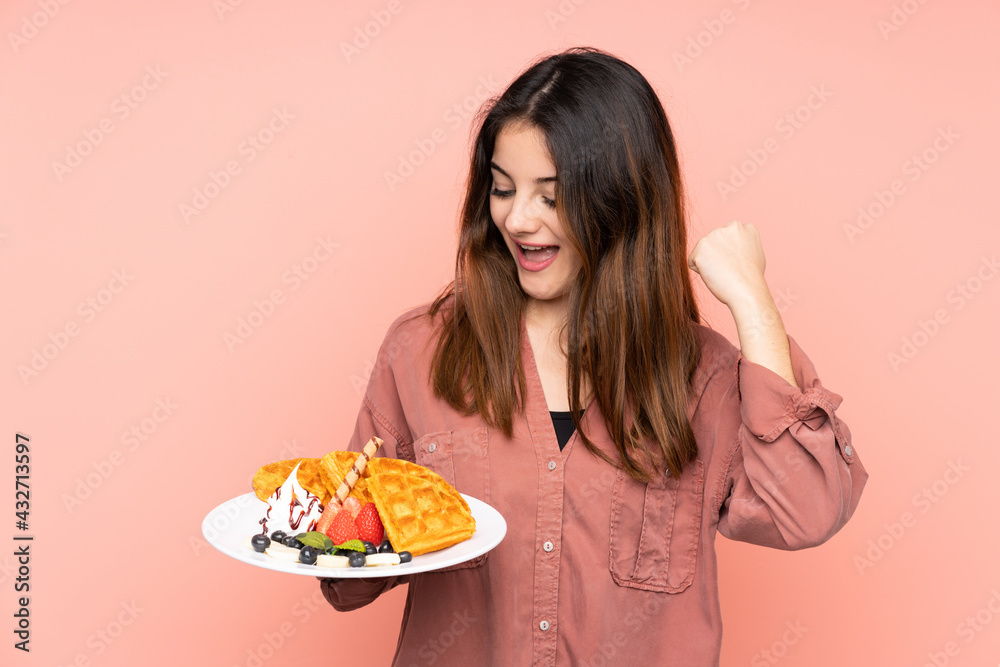 Young caucasian woman holding waffles isolated on pink background celebrating a victory