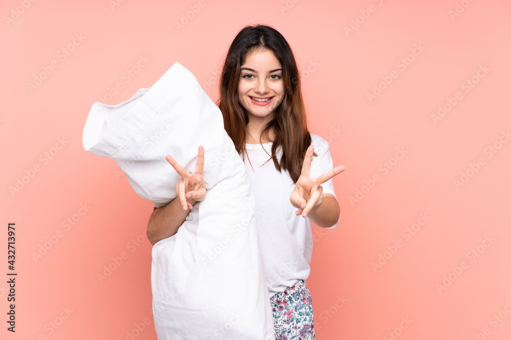Young woman in pajamas isolated on pink background smiling and showing victory sign Young woman in pajamas isolated on pink background smiling and showing victory sign
