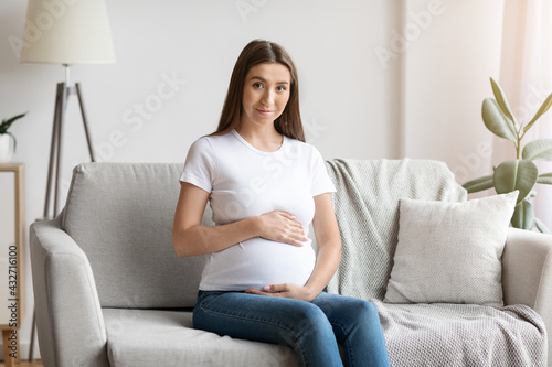 Happy Expectation. Portrait Of Beautiful Pregnant Woman Sitting On Couch At Home