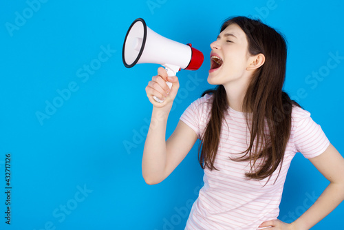 Funny young beautiful Caucasian woman wearing stripped T-shirt over blue wall People sincere emotions lifestyle concept. Mock up copy space. Screaming in megaphone.