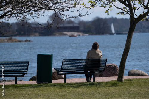 A woman sitting on a bench in the public park looking at the sea.