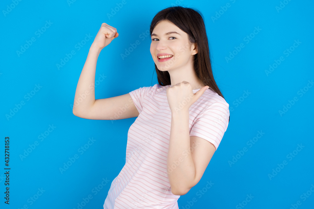 Fototapeta premium Hooray cool young beautiful Caucasian woman wearing stripped T-shirt over blue wall point back empty space hand fist