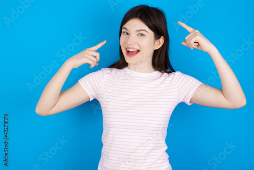 Cheerful young beautiful Caucasian woman wearing stripped T-shirt over blue wall demonstrating hairdo