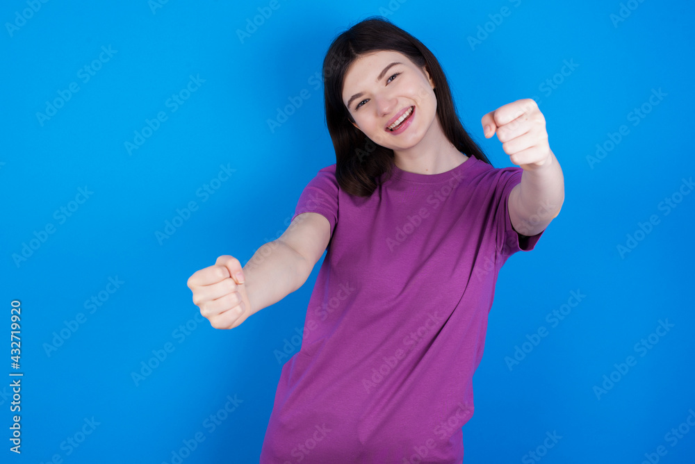 Fototapeta premium young beautiful Caucasian woman wearing purple T-shirt over blue wall imagine steering wheel helm rudder passing driving exam good mood fast speed