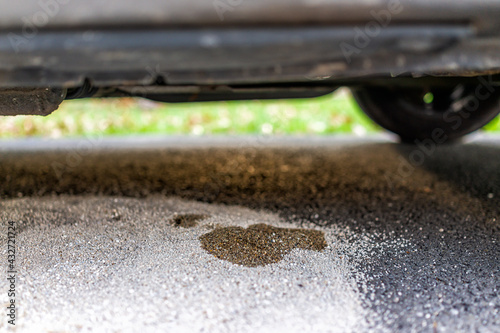 Parked car in driveway with macro closeup of vehicle leaking fuel on cat litter to prevent damaging pavement and to absorb the gas
