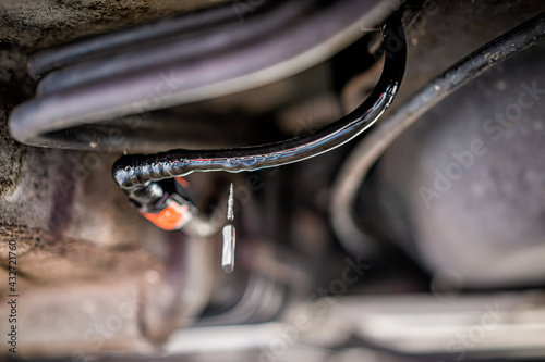 Macro closeup long exposure of vehicle leaking fuel liquid under car with texture of wet wires cables and falling drop. The wires were chewed by rodents causing the danger. photo