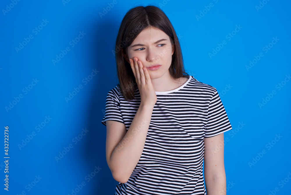 young beautiful Caucasian woman wearing stripped T-shirt over blue wall with toothache young beautiful Caucasian woman wearing stripped T-shirt over blue wall with toothache
