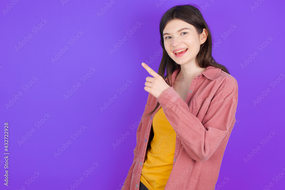 young beautiful Caucasian woman wearing blue T-shirt over blue wall pointing away and smiling to you. Look over there! young beautiful Caucasian woman wearing blue T-shirt over blue wall pointing away and smiling to you. Look over there!