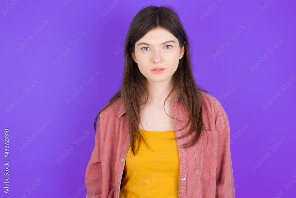 Joyful young beautiful Caucasian woman wearing casual clothes over purple wall looking to the camera, thinking about something. Both arms down, neutral facial expression. Joyful young beautiful Caucasian woman wearing casual clothes over purple wall looking to the camera, thinking about something. Both arms down, neutral facial expression.