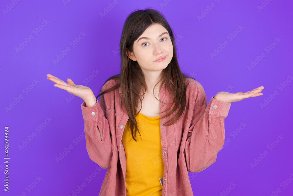 Puzzled and clueless young beautiful Caucasian woman wearing casual clothes over purple wall with arms out, shrugging shoulders, saying: who cares, so what, I don't know. Puzzled and clueless young beautiful Caucasian woman wearing casual clothes over purple wall with arms out, shrugging shoulders, saying: who cares, so what, I don't know.