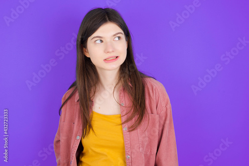 Oops! Portrait of young beautiful Caucasian woman wearing casual clothes over purple wall clenches teeth and looks confusedly aside, realizes her bad mistake,