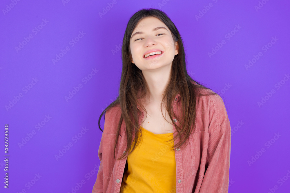young beautiful Caucasian woman wearing casual clothes over purple wall with broad smile, shows white teeth, feeling confident rejoices having day off. young beautiful Caucasian woman wearing casual clothes over purple wall with broad smile, shows white teeth, feeling confident rejoices having day off.