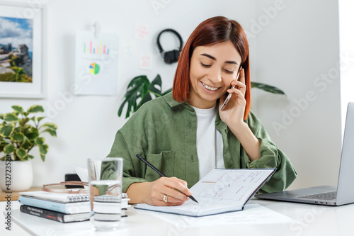 Woman remotely working at home with laptop computer. Young businesswoman talking by phone. Concept of online business or communication, home office and telework for entrepreneur
