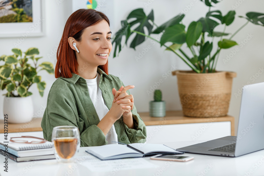 Woman remotely working at home with laptop. Young businesswoman talking via wireless earphones. Concept of online business or communication, freelance, home office and telework for entrepreneur Woman remotely working at home with laptop. Young businesswoman talking via wireless earphones. Concept of online business or communication, freelance, home office and telework for entrepreneur