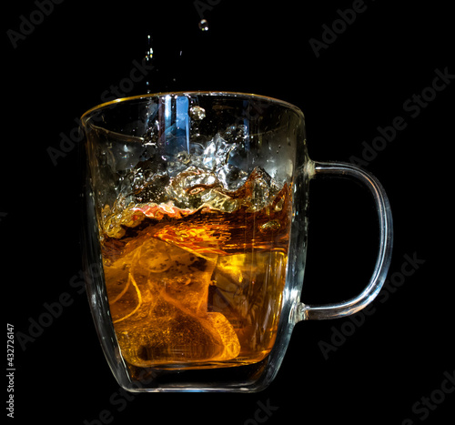 A tea bag fall into a glass mug with hot water, on a black background