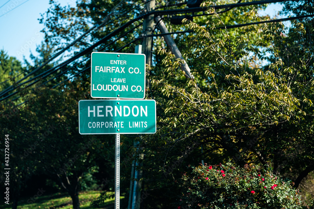 Road sign for city or town of Herndon corporate limits with enter Fairfax leave Loudoun county in Northern Virginia suburbs by green trees park near Washington DC