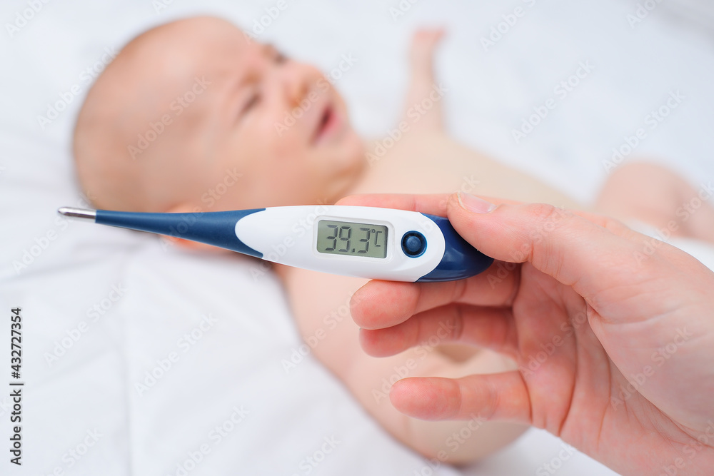 the hand of a mother or doctor holding a thermometer with a mark of 39.3 degrees on the background of a crying baby.