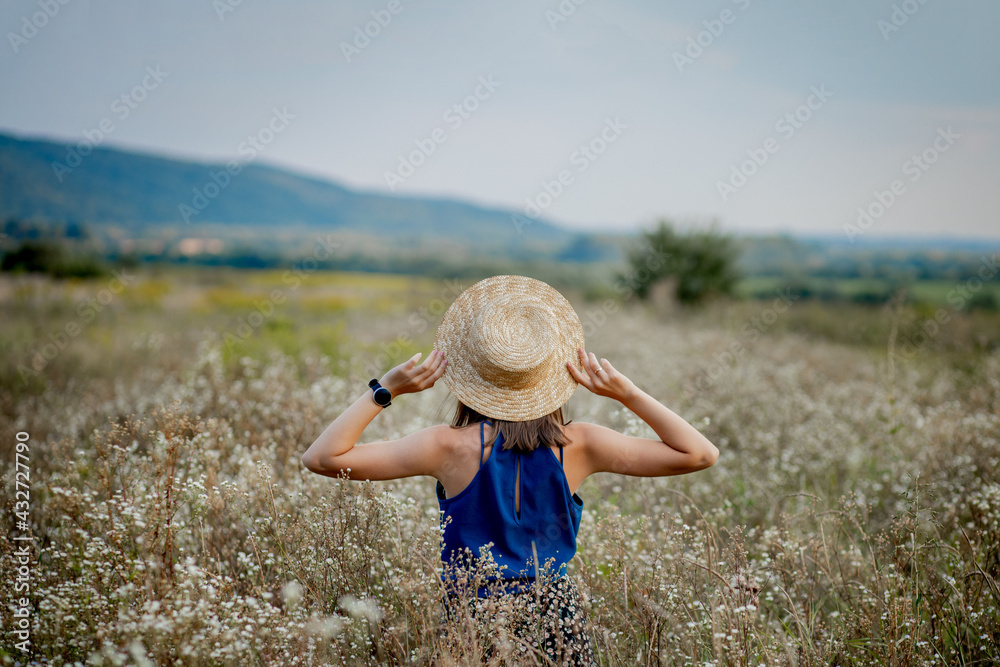 Woman Staying on Wildflowers Field Looking Away Copyspace. Smiling Attractive Young Girl Brunette Wearing Stylish Clothes and Hat Stay on Agricultural Flowers Valley. Cute Lady on Countryside Place