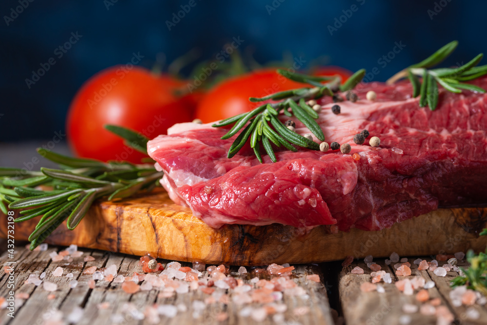 Grilled beef with vegetables. Preparation for the cooking process. Close-up. A piece of beef meat, tomatoes, herbs. Wooden plank. Delicious homemade food. Picnic and weekend food